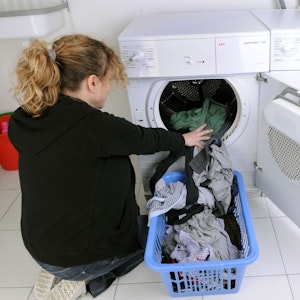 Eine Hausfrau befüllt einen Wäschetrockner mit frisch gewaschener Kleidung.