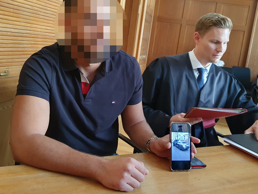 Kläger Onur M. (l) zeigt im Düsseldorfer Verwaltungsgericht sein Auto auf dem Display seines Smartphones. Der 22-Jährige ist mit Erfolg gegen ein von der Stadt angedrohtes Zwangsgeld für sogenanntes Autoposen vorgegangen.