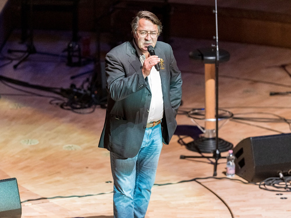 Hans Mörtter steht mit einem Mikrofon auf der Bühne der Kölner Philharmonie.
