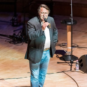 Hans Mörtter steht mit einem Mikrofon auf der Bühne der Kölner Philharmonie.