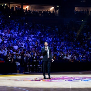 Dirk Nowitzki steht in der abgedunkelten Lanxess-Arena in Köln und hält mit Mikrofon eine Rede.