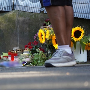 Zwei Menschen stehen an einem Zaun, an dem mit Kerzen und Blumen eines von der Polizei erschossenen Jugendlichen gedacht wird.
