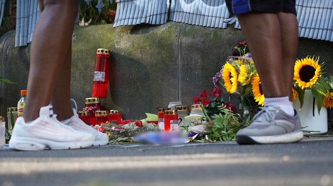 Zwei Menschen stehen an einem Zaun, an dem mit Kerzen und Blumen eines von der Polizei erschossenen Jugendlichen gedacht wird.