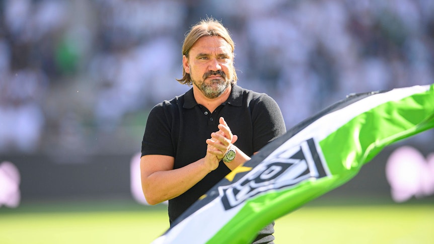 Trainer Daniel Farke bedankt sich nach dem Spiel von Borussia Mönchengladbach gegen die TSG Hoffenheim am 6. August 2022 bei den Fans im Borussia-Park. Farke applaudiert, im Vordergrund ist eine Fahne in den Gladbacher Vereinsfarben zu sehen.