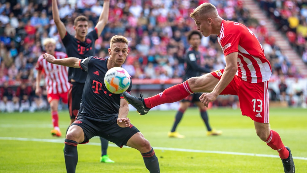 Berlins Andras Schäfer springt mit gestrecktem Bein zum Ball vor Joshua Kimmich von Bayern München.