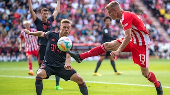 Berlins Andras Schäfer springt mit gestrecktem Bein zum Ball vor Joshua Kimmich von Bayern München. 