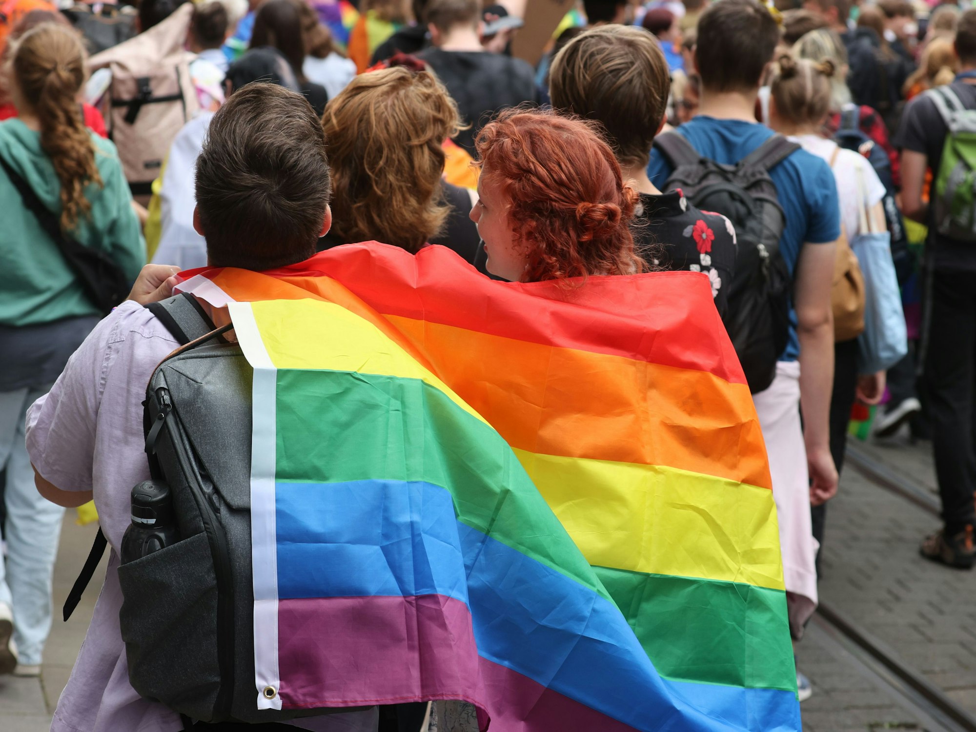 Menschen gehen beim Erfurter Christopher Street Day (CSD) für mehr Toleranz und Vielfalt in der Gesellschaft durch die Innenstadt, zwei Personen tragen gemeinsam eine Regenbogenfahne.