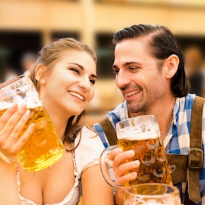 Zwei junge Menschen in Dirndl und Tracht genießen ein Bier auf dem Oktoberfest.