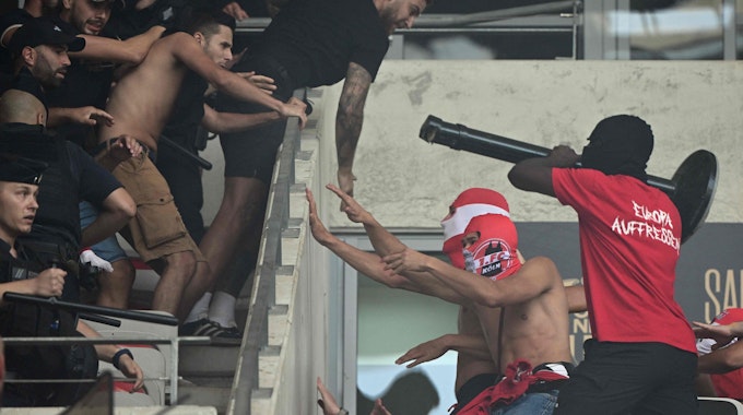 Maskierte Hooligans des 1. FC Köln nähern sich Anhängern vom OGC Nizza auf der Tribüne. Ein Kölner versucht, mit einem Absperrpfosten nach den Heimfans zu schlagen.