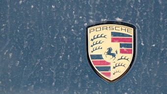 Ein Logo des Fahrzeugbauers Porsche ist an einer mit Wüstenstaub bedeckten Motohaube eines Sportwagens angebracht. 