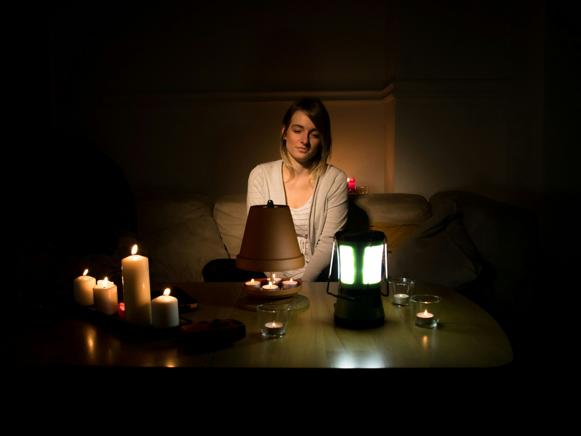 Eine Frau sitzt nach einem Stromausfall bei Kerzenlicht auf einem Sofa.