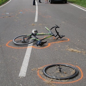 Der Vorderreifen eines Fahrrads liegt neben dem Fahrrad an einer Unfallstelle. Beides ist mit Markierungen der Polizei gekennzeichnet.