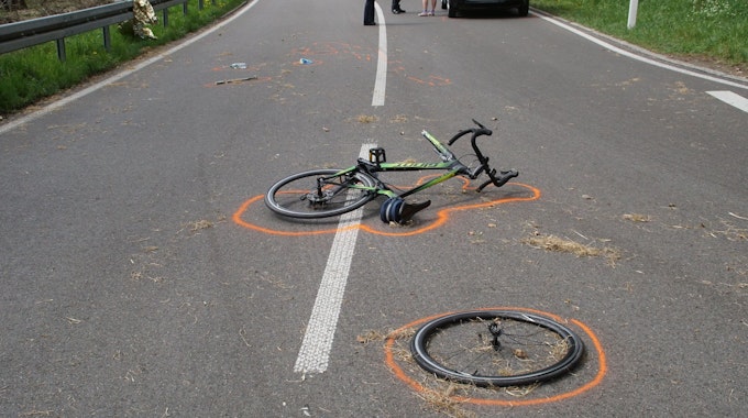 Der Vorderreifen eines Fahrrads liegt neben dem Fahrrad an einer Unfallstelle. Beides ist mit Markierungen der Polizei gekennzeichnet.