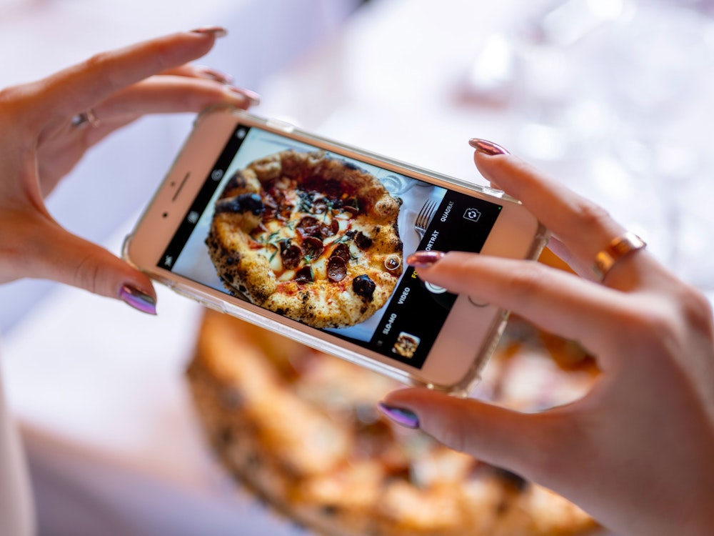 Eine Frau fotografiert mit ihrem Smartphone eine Pizza.
