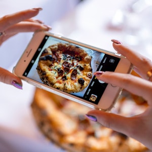 Eine Frau fotografiert mit ihrem Smartphone eine Pizza.