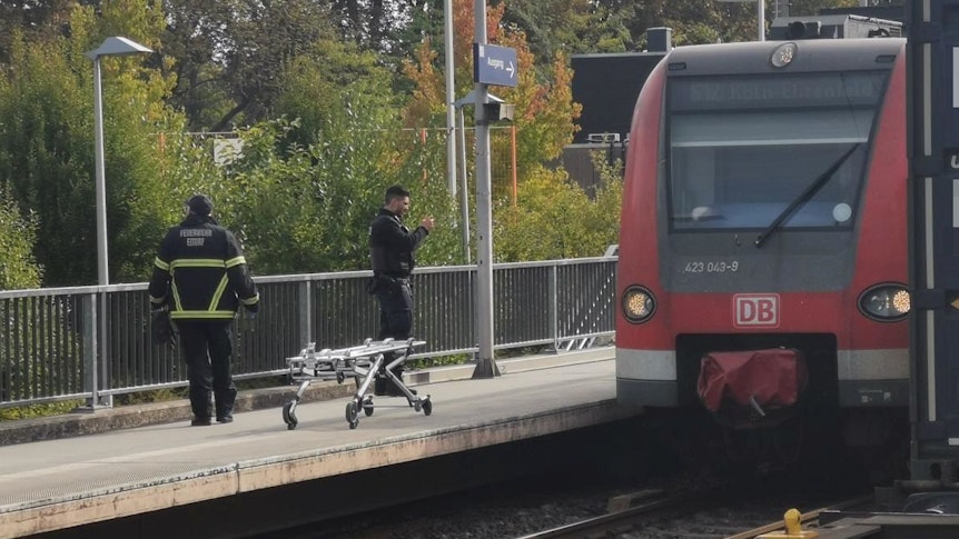 Zwei Einsatzkräfte stehen am Gleis, an dem ein Zug hält.