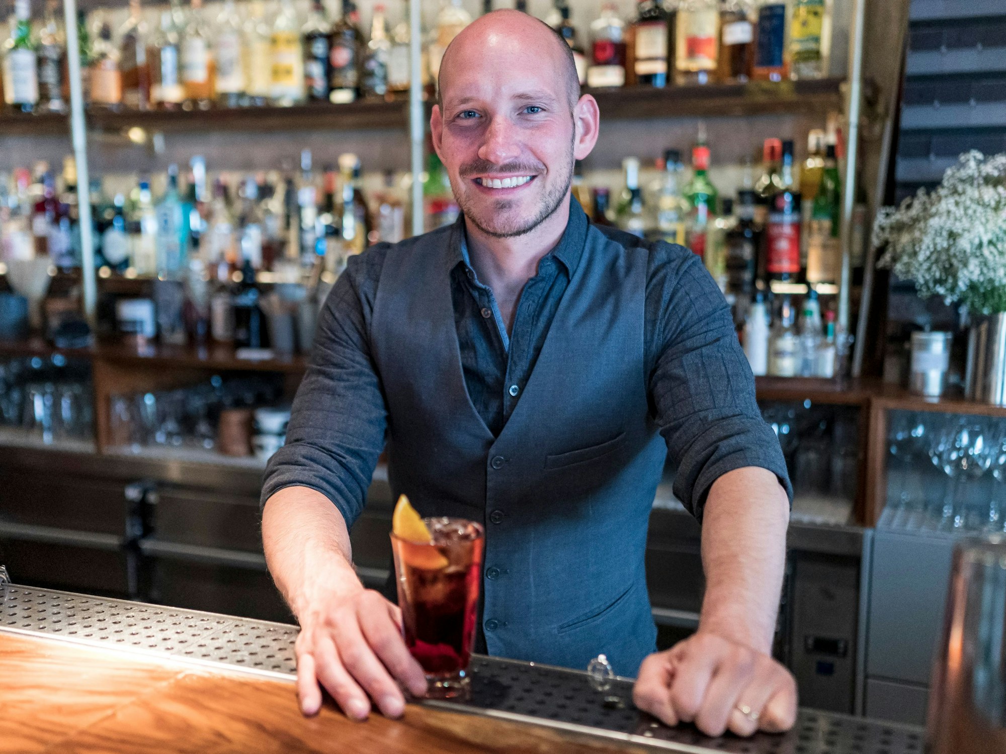 Suderman-Chef Felix Engels lächelt mit einem Cocktail in der Hand in die Kamera.