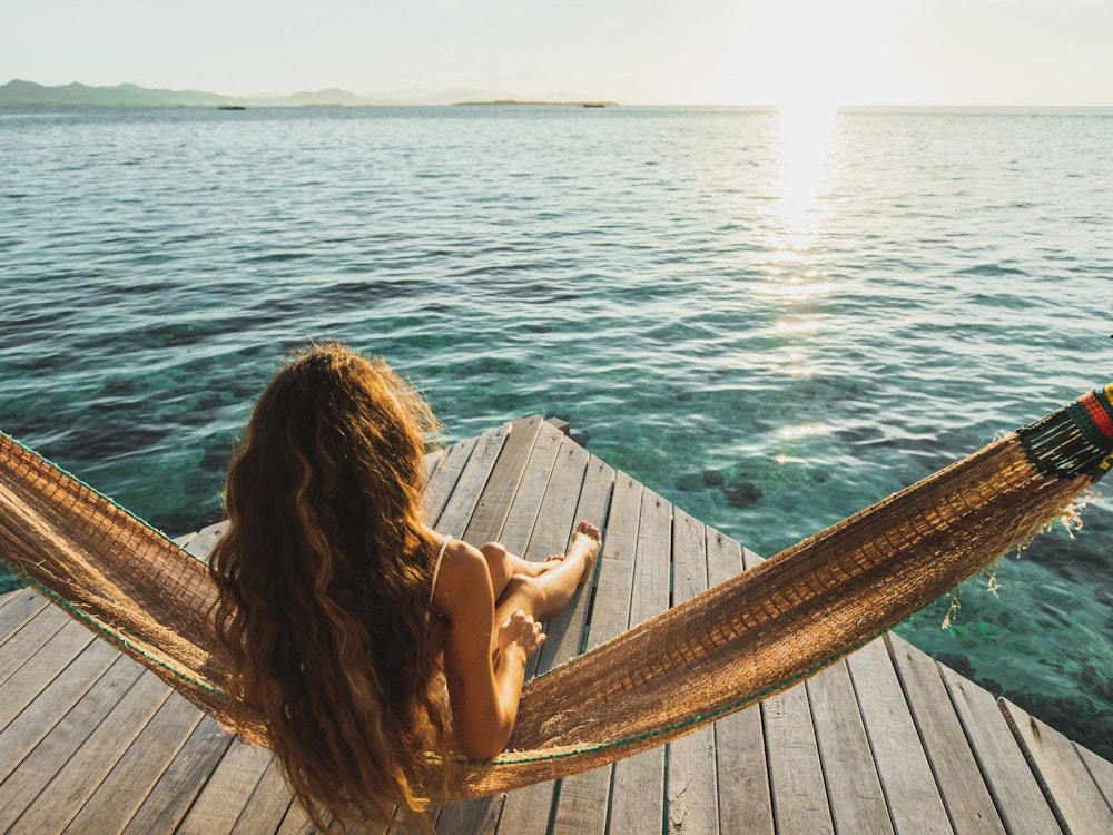 Frau im Bikini blickt über das Meer Richtung Sonnenuntergang. Bild zum Urlaubs Reiseveranstalter Artikel.