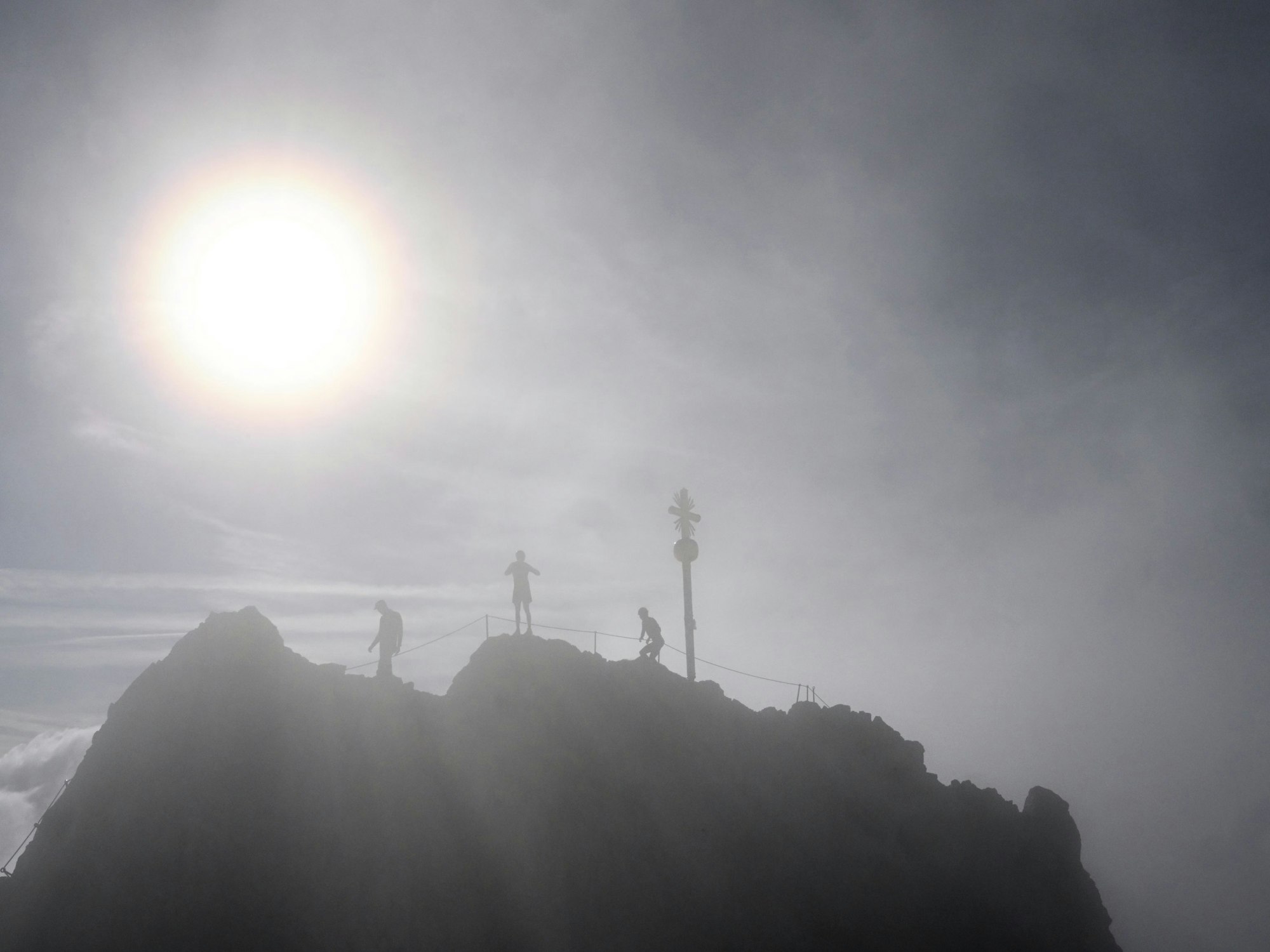 Drei Bergsteiger stehen neben dem Gipfelkreuz der Zugspitze.