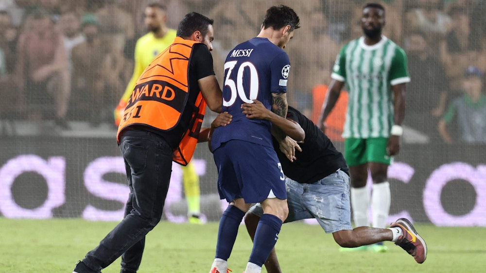 Ein Flitzer umarmt Lionel Messi während des Spiels von Paris St. Germain bei Maccabi Haifa. Ein Ordner versucht die beiden voneinander zu trennen.