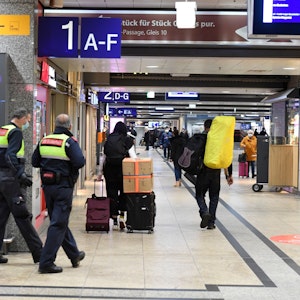 Reisende und Sicherheitskräfte gehen im Hauptbahnhof durch einen Gang zu den Bahnsteigen.