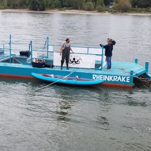 Ein blauer Ponton schwimmt auf dem Rhein bei Köln. Damit wird Müll aus dem Wasser gefischt.