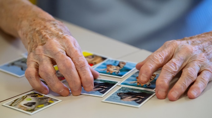 Das undatierte Symbolfoto zeigt die Hände eines alten Menschen und Memory-Karten auf einem Tisch.