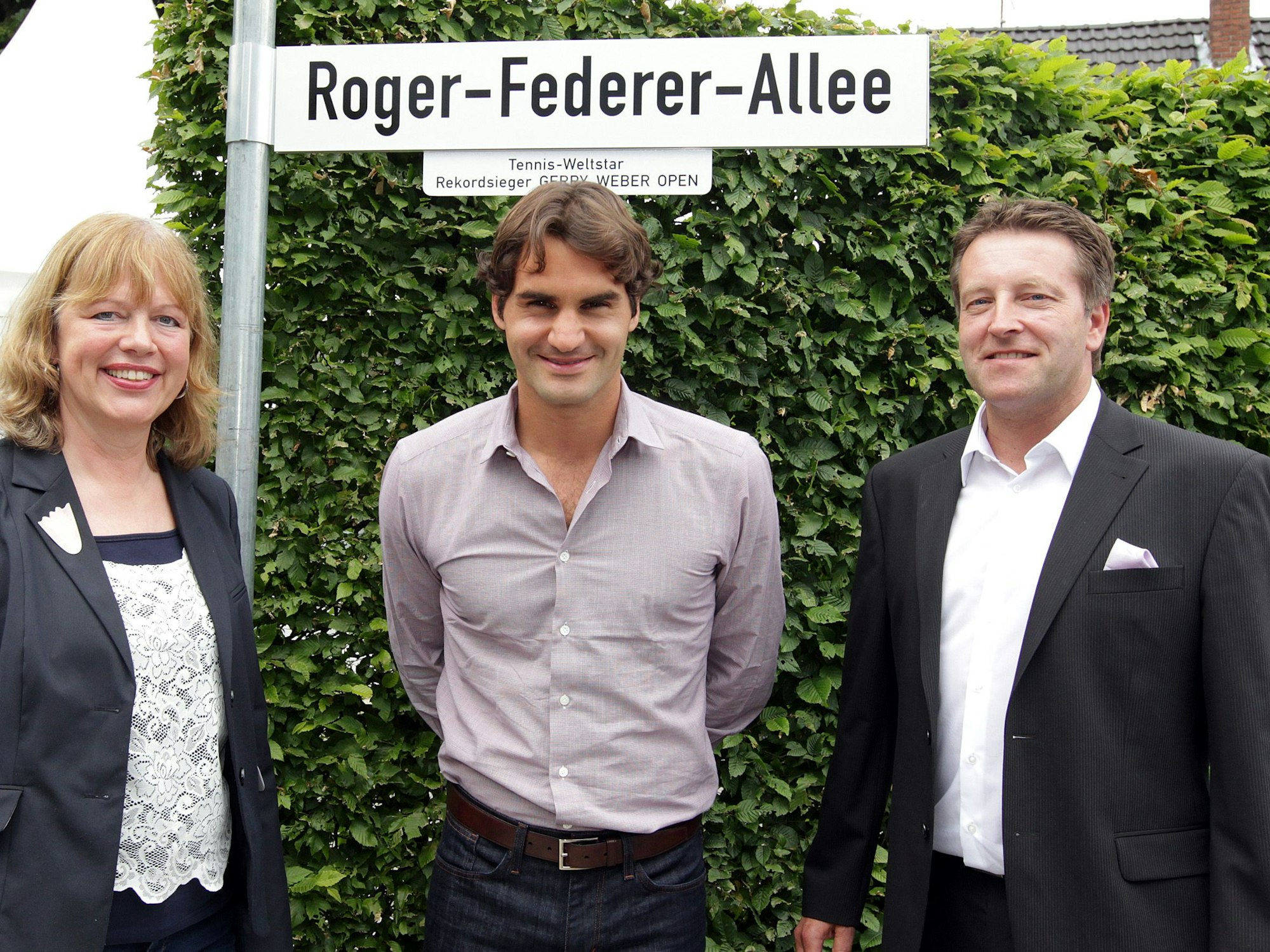 Anne Wesselmann, Roger Federer und Ralf Weber stehen vor dem Straßenschild zur „Roger-Federer-Allee“.