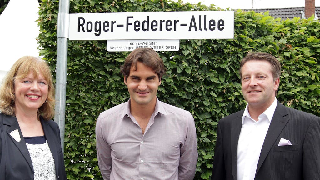 Anne Wesselmann, Roger Federer und Ralf Weber stehen vor dem Straßenschild zur „Roger-Federer-Allee“.