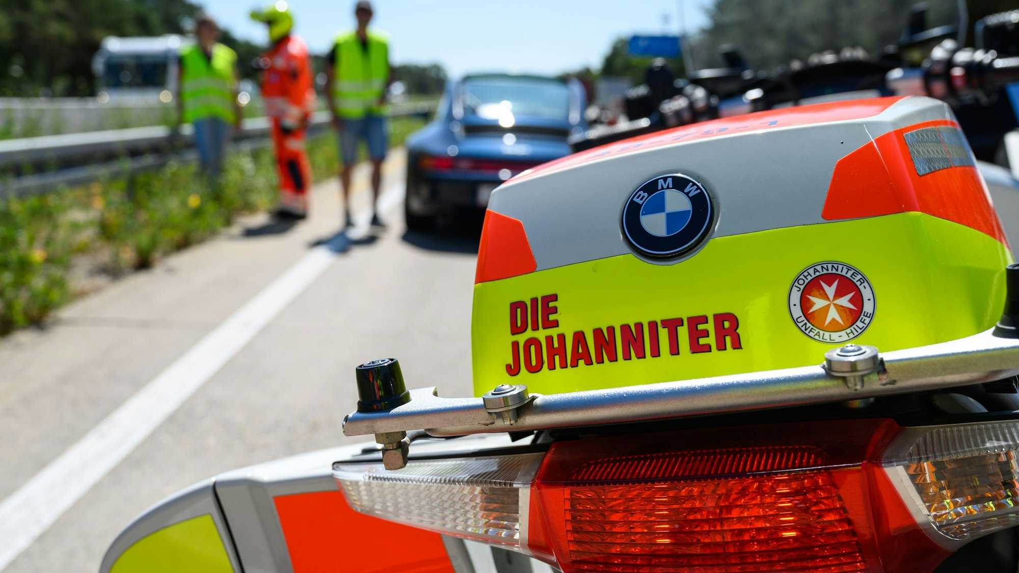Ein Johanniter-Stauhelfer steht mit seinem Motorrad auf der Autobahn und hilft einem liegengebliebenen Autofahrer.
