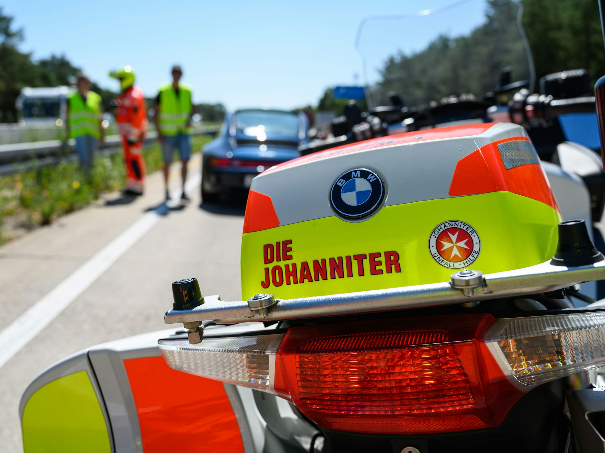 Ein Johanniter-Stauhelfer steht mit seinem Motorrad auf der Autobahn und hilft einem liegengebliebenen Autofahrer.