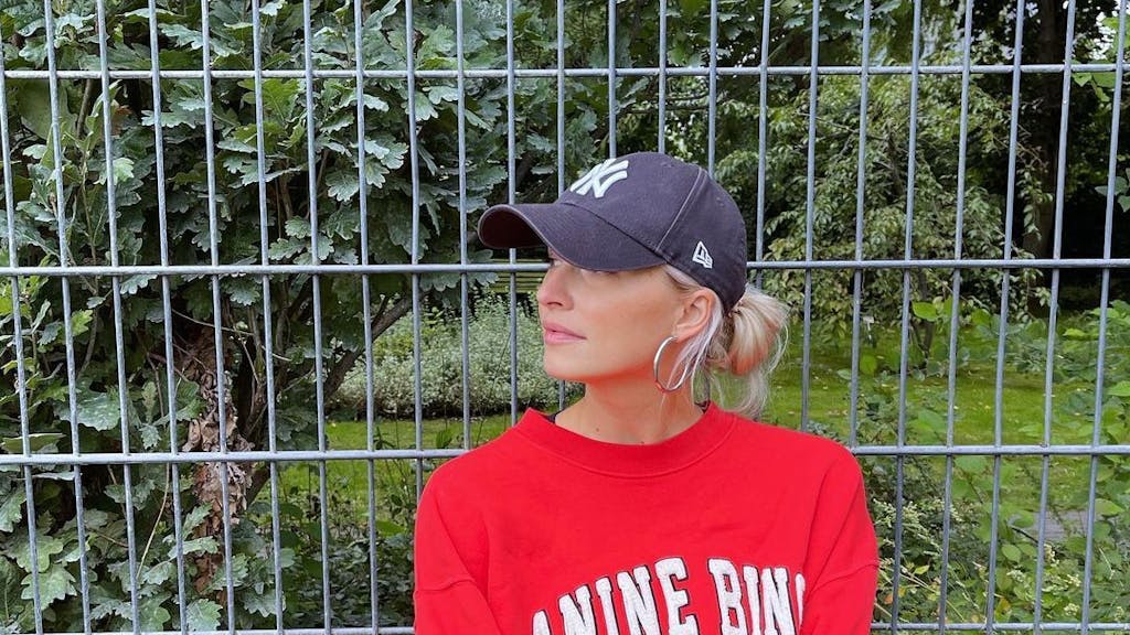 Moderatorin Lena Gercke, hier auf einem Instagram-Foto von September 2022, begeistert mit Babybauch-Beitrag ihre Fans auf Instagram. Auf dem Foto sitzt Lena vor einem Zaun. Sie trägt einen roten Pullover und ein schwarzes Käppi.