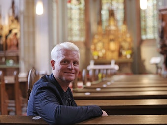 Guido Cantz sitzt in der Kirche St. Aegidius in Köln und schaut über die Schulter in die Kamera.