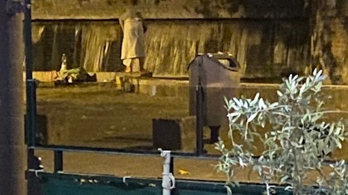 Eine Frau steht neben einem öffentlichen Brunnen mit einem Badetuch.