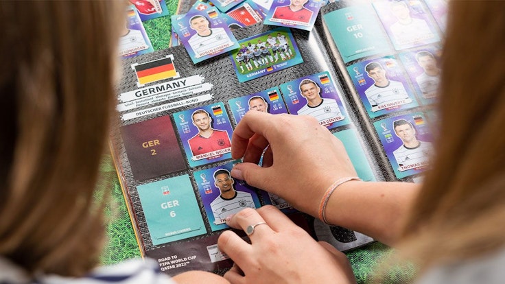 Zwei Mädchen sitzen am Tisch und kleben Panini-WM-Sticker der deutschen Fußball-Nationalmannschaft in das FIFA World Cup 2022 Qatar Stickeralbum ein.