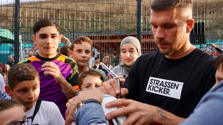 Lukas Podolski bei der Eröffnung eines Bolzplatzes von den Fans umringt.