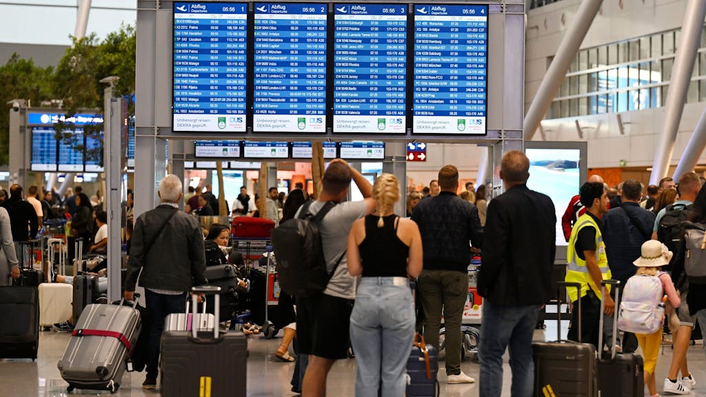 Menschen stehen vor einer Anzeigetafel am Flughafen Düsseldorf und checken ihre Flüge.