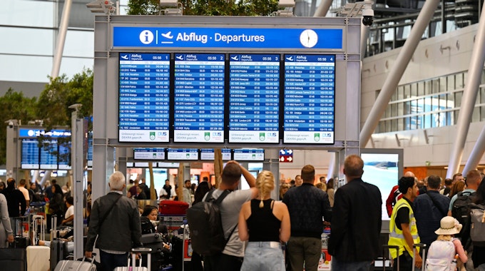 Menschen stehen vor einer Anzeigetafel am Flughafen Düsseldorf und checken ihre Flüge.