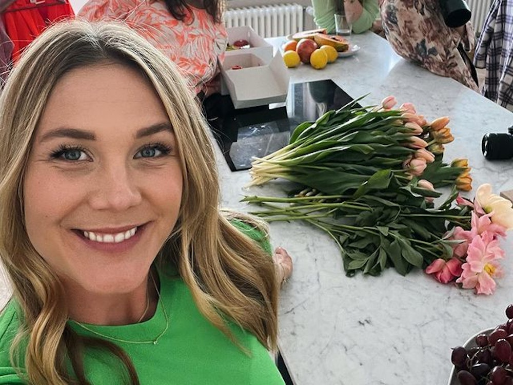 Alina Merkau macht ein Selfie. Im Hintergrund stehen drei weitere Frauen. Hinter ihr auf der Küchenarbeitsplatte liegen verschiedene Blumen.