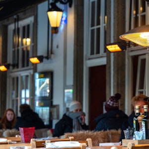 Restaurantbesucher sitzen im Winter unter Wärmelampen in der Außengastronomie.