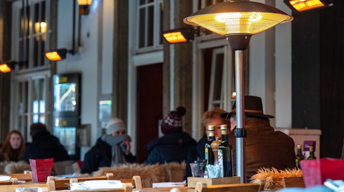 Restaurantbesucher sitzen im Winter unter Wärmelampen in der Außengastronomie.