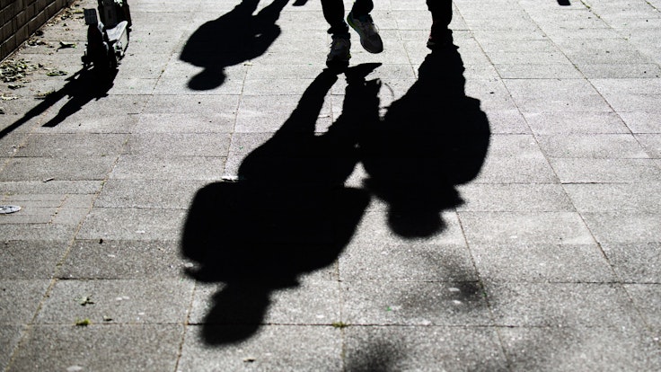 Schüler gehen am Morgen zur Schule und werfen dabei ihre Schatten auf den Gehweg.