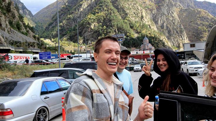 Eine Gruppe von Russinnen und Russen lächelt am Grenzübergang Werchni Lars zwischen Georgien und Russland am Freitag (23. September 2022). Auch dort haben sich lange Fahrzeugschlangen gebildet, nachdem Putin eine Teilmobilisierung in seinem Land angekündigt hatte.