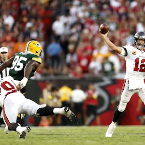 Tom Brady (r.) wirft einen Football, während ein Gegenspieler der Green Bay Packers versucht, ihn daran zu hindern.