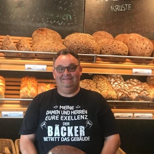Bäcker Gudio Boveleth steht in seiner Bäckerei vor einem Brotregal.