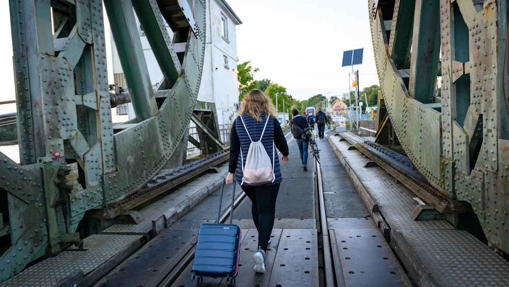 Eine Frau läuft mit einem Koffer über die Lindaunisbrücke. Normalerweise fahren Züge über die Schleibrücke bei Lindaunis. Seit Mitte September aber heißt es für Fahrgäste: Austeigen und zu Fuß die Schlei passieren.