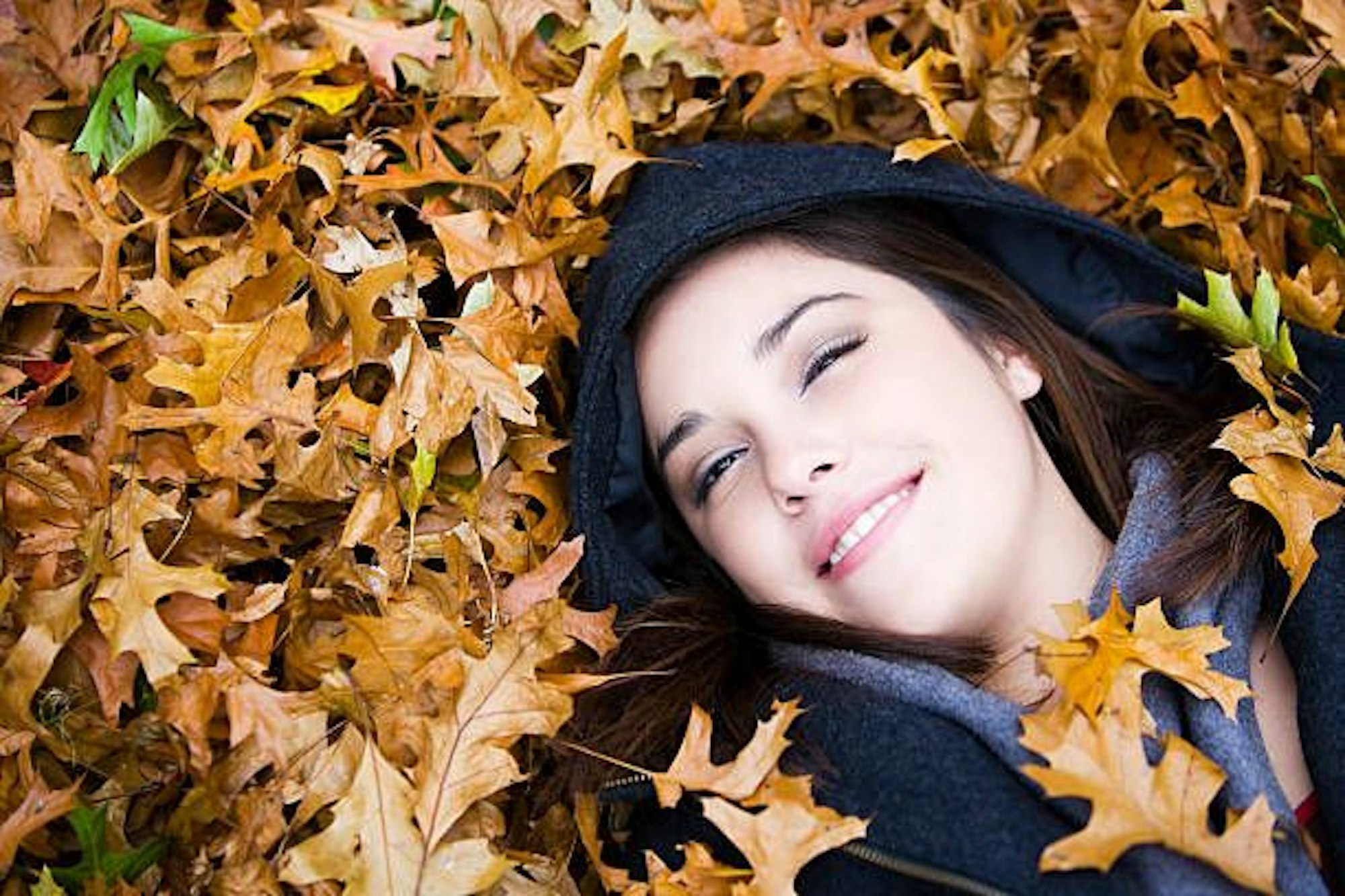 Eine Frau liegt im Herbstlaub und lächelt.
