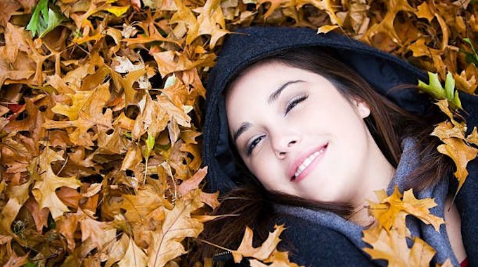 Eine Frau liegt im Herbstlaub und lächelt.&nbsp;