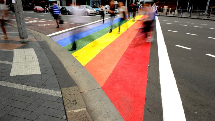 Menschen gehen über einen Zebrastreifen in den Farben des Regenbogens.