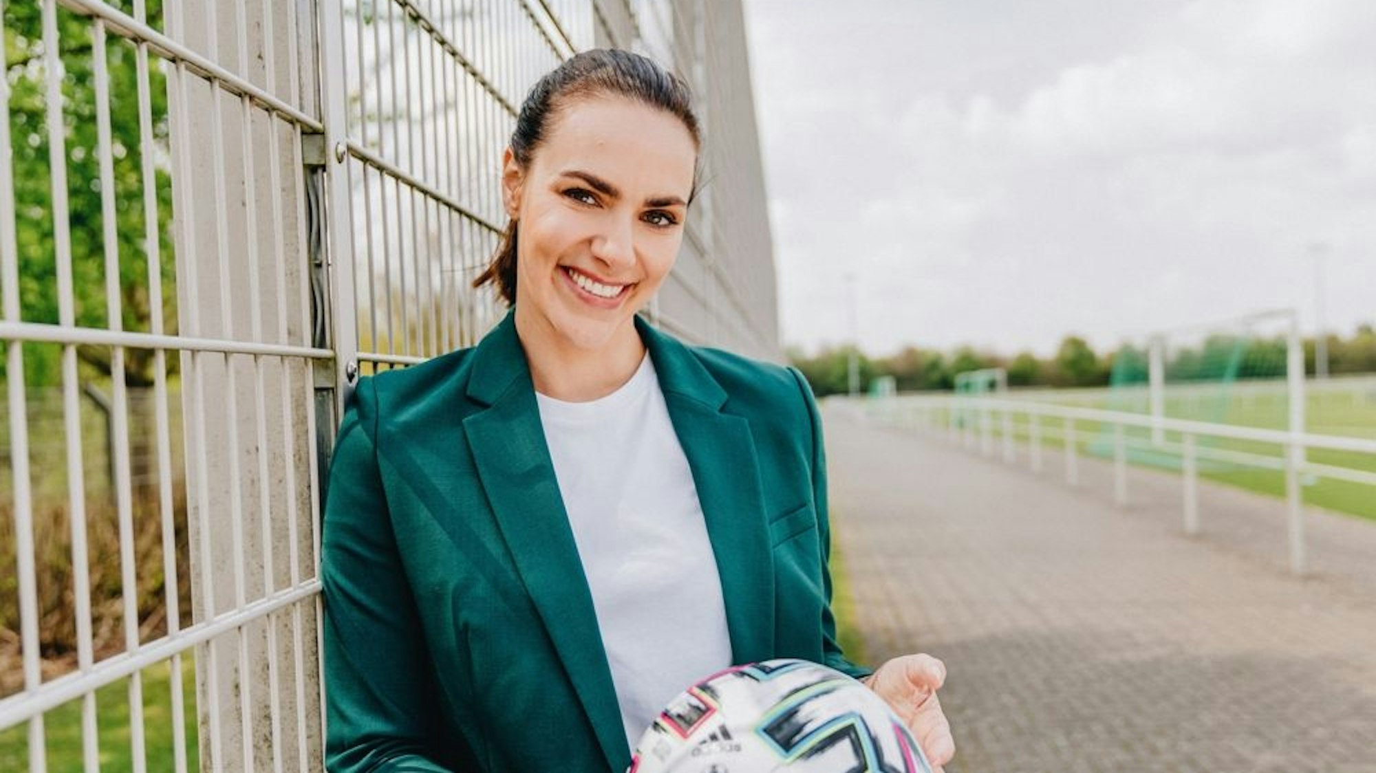 Esther Sedlaczek hält lachend einen Fußball in der Hand.